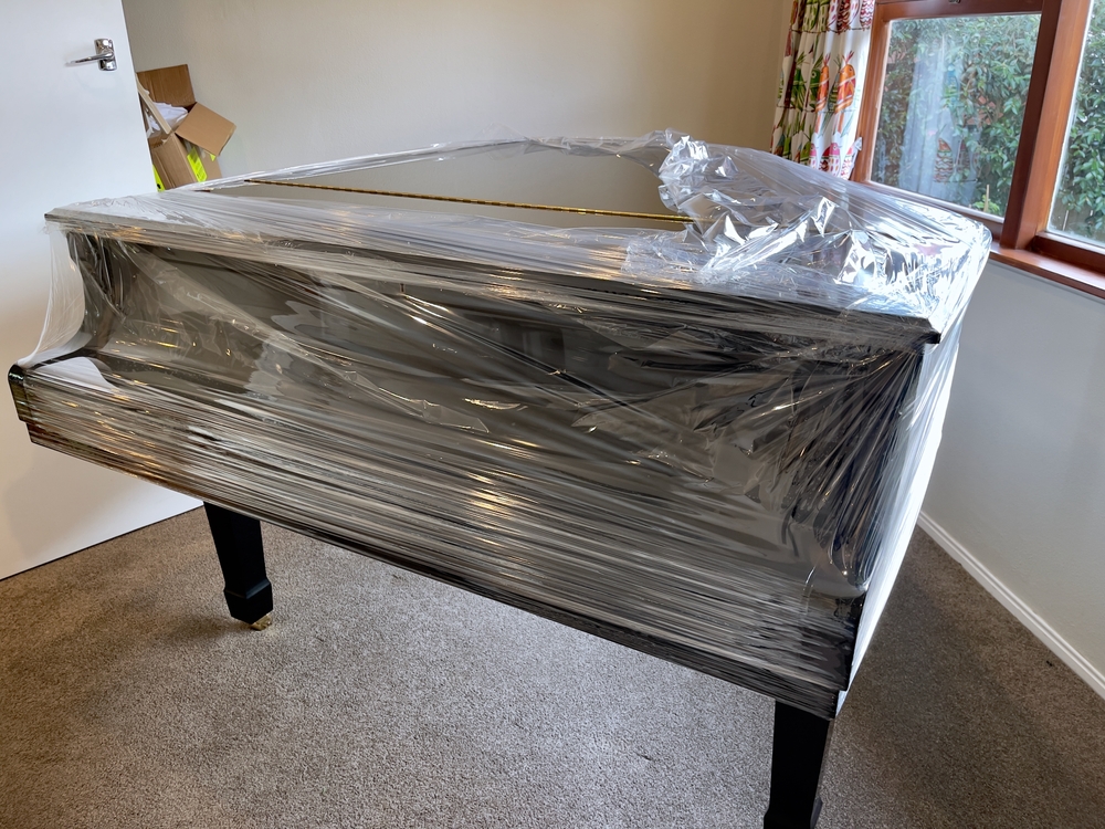 Glossy,black,grand,piano,partially,covered,in,plastic,wrap,in
